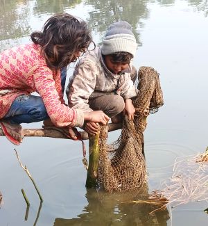 कड़ाके की ठंड में तालाब के ठंडे पानी में जाल से मछली पकड़ते ग्रामीण बच्चे, सर्द मौसम में फिशिंग करते हुए मेहनत और संघर्ष की झलक दिखाती तस्वीर