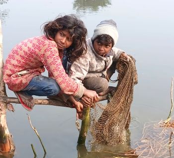 कड़ाके की ठंड में तालाब के ठंडे पानी में जाल से मछली पकड़ते ग्रामीण बच्चे, सर्द मौसम में फिशिंग करते हुए मेहनत और संघर्ष की झलक दिखाती तस्वीर